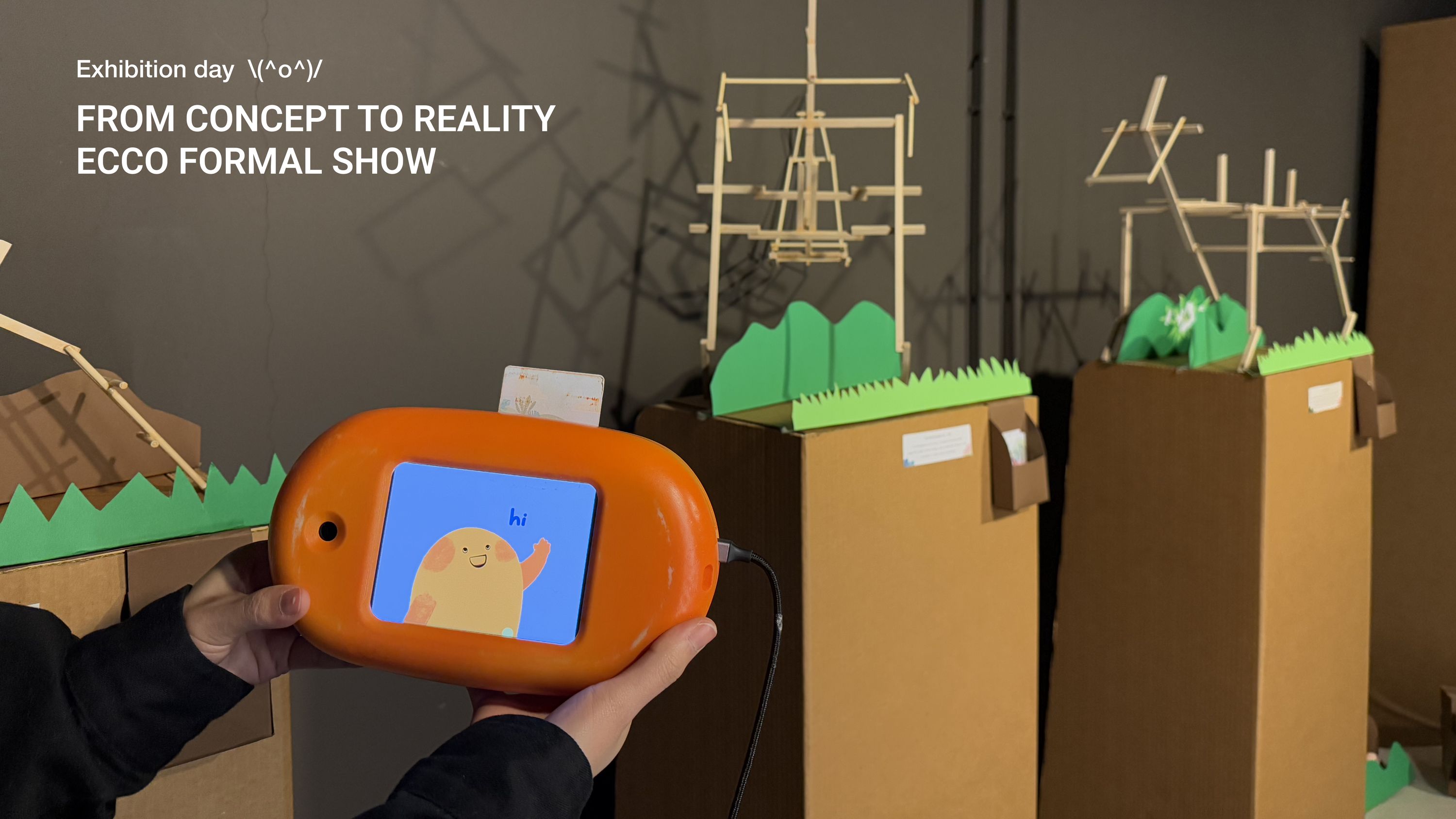 Exhibition day photograph, from concept to reality, the Ecco formal show, with the finished orange device held in front of a constructed cardboard and timber dinosaur exhibit